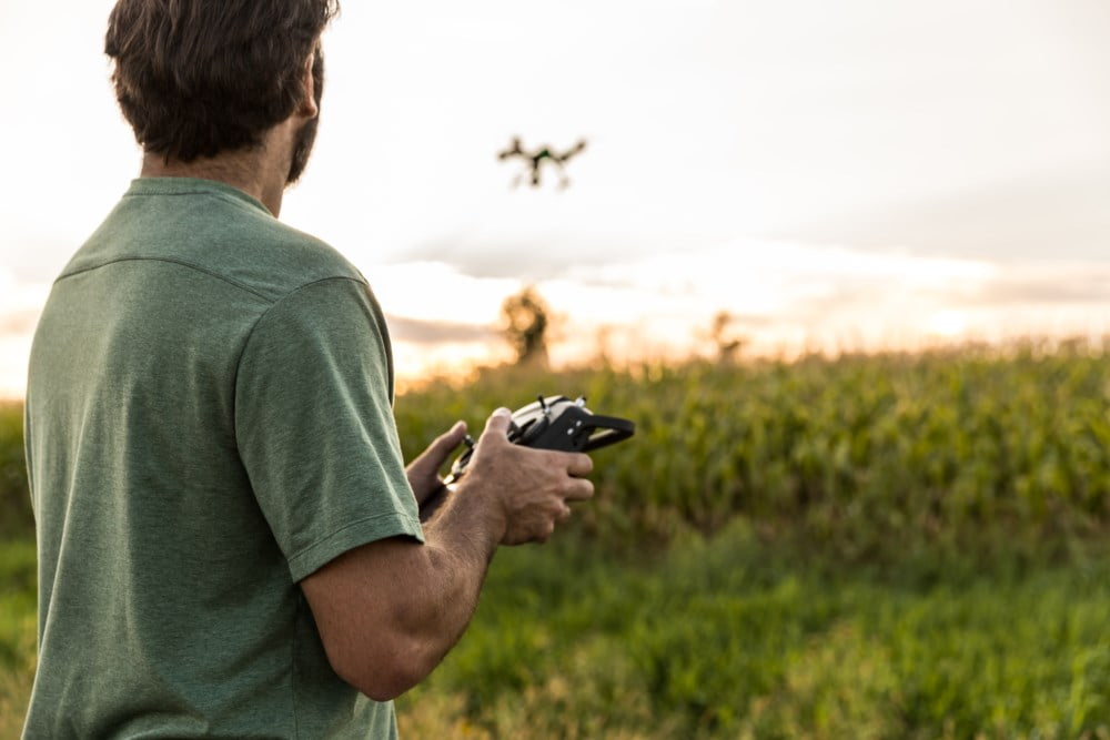 Mann i grønn t-skjorte flyr drone over en åker